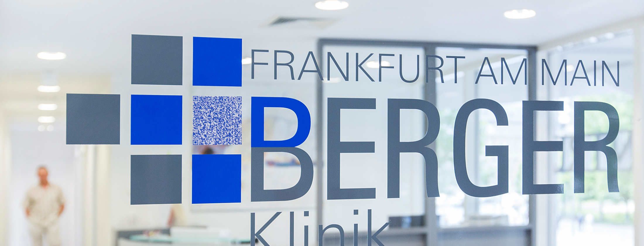 Firmenlogo auf der Glastür zum Empfangsbereich der Berger Klinik Frankfurt. Das Logo ist durch einen QR-Code ergänzt. Per Mobile kann nun ein Besucher alle Informationen auf sein Handy laden und hat die Kontaktdaten des Operationszentrums aus Westend.