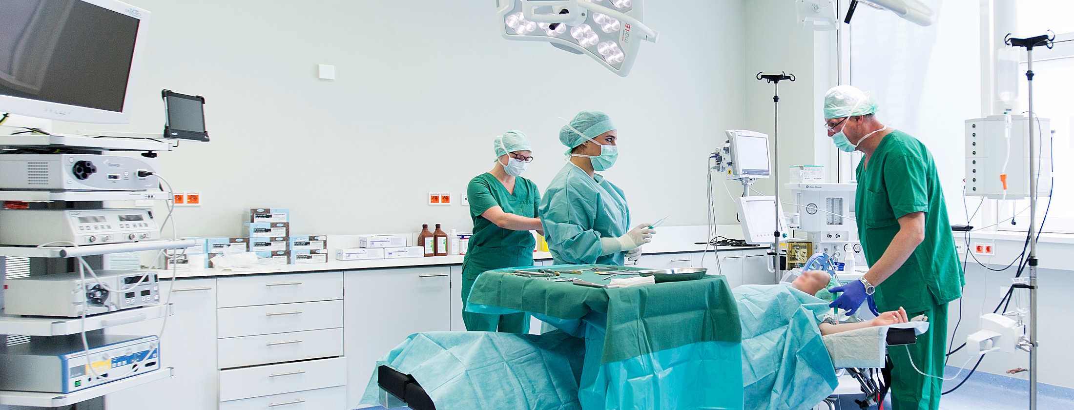 Ein modern ausgestatteter Operationsraum der Berger Klinik für internationale Patienten in Deutschland. Eine Patientin liegt auf dem OP-Tisch. Rundherum steht medizinisches Fachpersonal und ein Schönheitschirurg. Operation verläuft ohne Komplikationen.