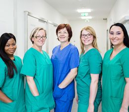 Пять сотрудников клиники стоят одеты в медицинские халаты в коридоре больницы. Фельдшер, медсестры, техник стерилизации, операционная техническая помощница помогают профессиональным хирургам в доме на Майнцер Ландштрассе, Франкфурт на Майне в Германии.