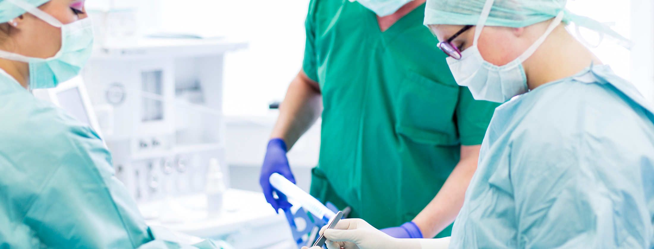 Schönheitschirurgen bei einer Schönheitsoperation in Frankfurt am Main. Operationsschwestern und der Plastische Chirurg sind in OP-Kittel gekleidet. Ein Anästhesiologe hält die Patienten im Tiefschlaf, während der Chirurg mit OP-Instrumenten hantiert.